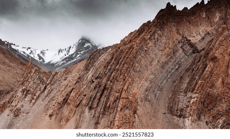 Perfectly visible fold structures in foreground and background with dark clouds and snow, Saach Pass, India.