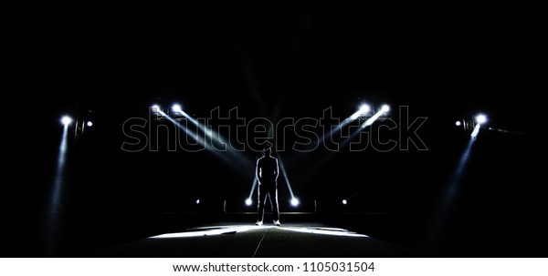 在建筑光束上的性能移动照明向下射线到舞台上的人作为领导者超级巨星 男性轮廓环绕光 暗暗低曝光 概念独特的信心库存照片 立即编辑
