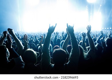 Performance Of A Popular Group. The Crowd With Raised Hands Against The Stage Light