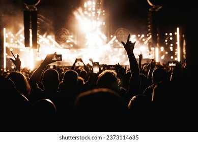 Performance of a popular group. The crowd with raised hands against the stage light.