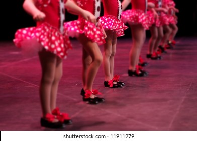 Performing on stage, a group of young dancers show off their talent and bright costumes - image highlights a narrow depth of field on the girl in the middle of the line