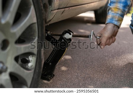 Performing tire change using jack on roadside during daylight with visible tools and focused individual