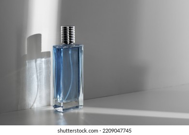 Perfume Bottle With Blue Liquid Casts Shadow On White Wall In Studio Closeup. Male Fragrance Demonstration. Glamorous Scent For Men