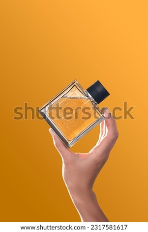 Perfume bottle in hands on an orange background.