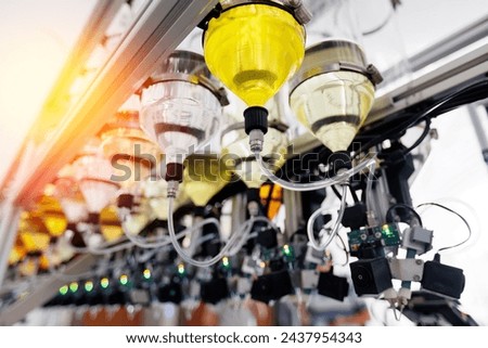 Perfume manufacturing process, overhead view of high tech filling bottles of aroma oil assembly line with yellow liquid of cosmetic.