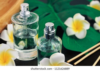 Perfume In Spray Bottles, Dark Black Background With Tropical Leaf And Flowers Decor. Aromatherapy Spa Treatment And Sensual Scents.