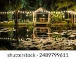 Pergola with glowing lights by the water. Gazebo with lights by the lake in late evening. Romantic scene in dusk. Patio romantic in the evening. Night gazebo, pavilion garden at night