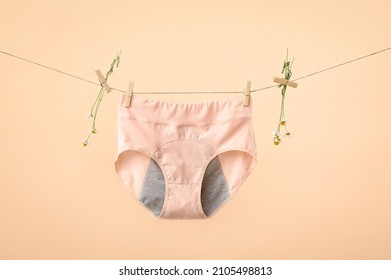 Period panties and chamomile flowers hanging on rope against color background
