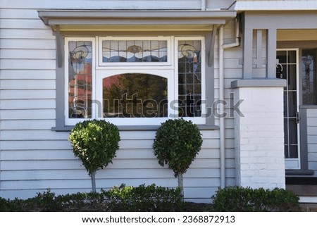 PERIOD TIMBER HOME WITH A  COVERED PORCH A classic old style gray wooden siding house with a covered patio verandah awning with decorative floral design leadlight windows and round topiary tree garden