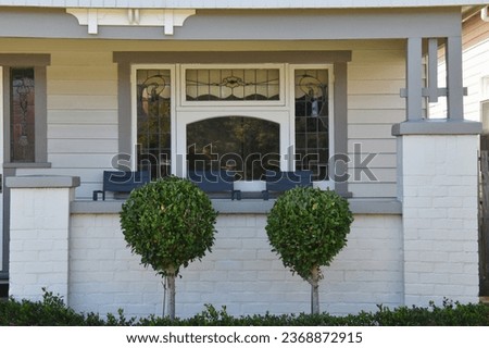 PERIOD TIMBER HOME WITH A  COVERED PORCH A classic old style gray wooden siding house with a covered patio verandah awning with decorative floral design leadlight windows and round topiary tree garden