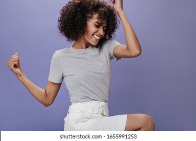 Perky woman in gray t-shirt laughs on purple background. Cheerful girl in white shorts dancing and jumping on isolated backdrop - Shutterstock ID 1655991253