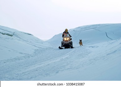 PERM, RUSSIA - FEBRUARY 24, 2018: man is riding a snowmobile among the hummocks, accompanied by a running dog
