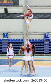 Perm, Russia - March 28, 2015. Championship Perm Krai On Cheerleading.  Girl In  Pink  And White Suit  Makes Element Bow And Arrow In Group Stunt