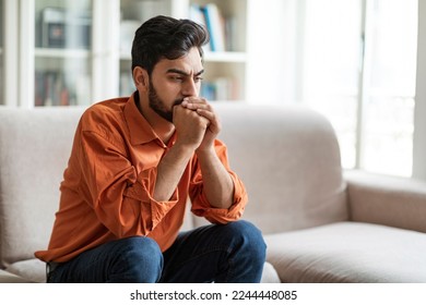 Permacrisis, life problems, financial hangout concept. Pensive young middle eastern man sitting on sofa at home, leaning on his hands, experiencing difficulties in life, looking at copy space - Powered by Shutterstock