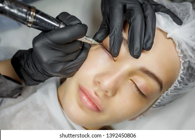 Permanent make up eyeliner procedure, applying on young girl. Close-up. Young beautiful woman making permanent makeup in cosmetology salon. Young girl applying permanent eyeliner in beauty studio