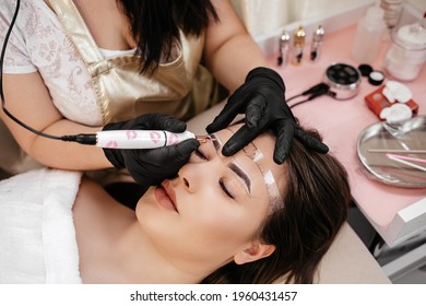Permanent make up on eyebrows of young woman by professional cosmetologist in a beauty salon.