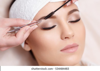 Permanent makeup. Beautiful young woman gets eyebrow correction procedure. Young woman tweezing her eyebrows in beauty saloon. Young woman plucking eyebrows with tweezers close up