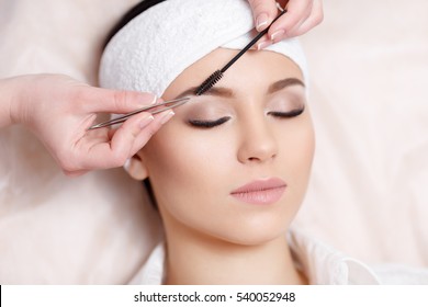 Permanent Makeup. Beautiful Young Woman Gets Eyebrow Correction Procedure. Young Woman Tweezing Her Eyebrows In Beauty Saloon. Young Woman Plucking Eyebrows With Tweezers Close Up