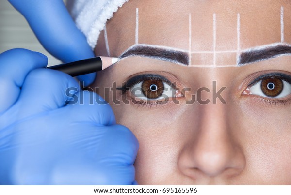 Permanent make-up for eyebrows of beautiful\
woman with thick brows in beauty salon. Closeup beautician doing \
tattooing eyebrow.