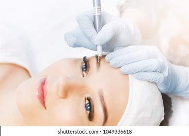 Permanent Makeup For Eyebrows. Microblading brow. Beautician Doing Eyebrow Tattooing For Female Face. Beautiful young girl in a beauty salon. Close up view of blue eyes with long eyelashes.