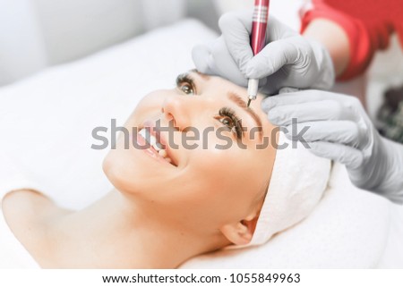 Permanent Makeup For Eyebrows. Microblading brow. Beautician Doing Eyebrow Tattooing For Female Face. Beautiful young girl in a beauty salon. Close up view of brown eyes with long eyelashes.