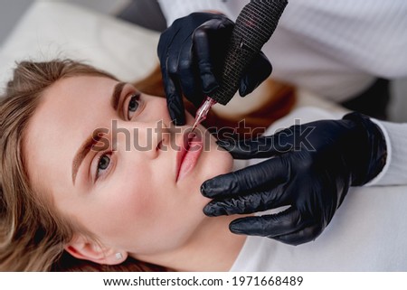 Permanent makeup master conturing lips in beauty salon. Side closeup view of tattoo process
