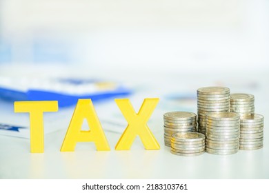 Peronal income tax, pay self assessment tax bill, financial concept : Yellow wood alphabet letters TAX, coin stacks on a table, depicting a taxpayer computes and prepares to pay personal income tax.