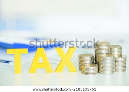 Peronal income tax, pay self assessment tax bill, financial concept : Yellow wood alphabet letters TAX, coin stacks on a table, depicting a taxpayer computes and prepares to pay personal income tax.