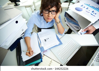 Perplexed accountant doing financial reports being surrounded by huge piles of documents