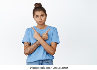 Perplexed Girl Deciding Between Two Options, Pointing Sideways And Looking At Right Side, Standing Over White Background