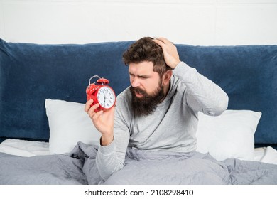 Perplexed Guy Scratching Head Holding Alarm Clock Being In Bed In Morning, Oversleep