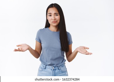 Perplexed and indecisive, skeptical cute asian girl cant decide, shrugging with hands spread sideways, smirk and look camera doubtful, not sure, puzzled to give answer, standing white background - Shutterstock ID 1632374284