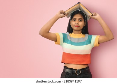 Perplexed and indecisive, skeptical cute indian asian girl posing isolated holding book on her head and looking directly to camera with copy space.