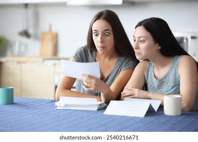 Perplexed interracial roommates checking strange bill in the kitchen at home