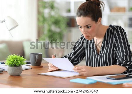 Perplexed self employed reading paper document in a wooden dekstop working at home