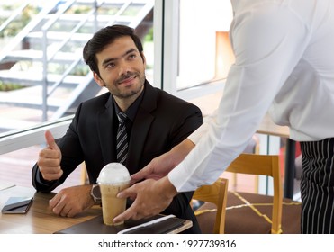 A Persian businessman in a black suit smiles and thumbs up after receiving iced coffee from the waiter. Atmosphere during lunch break in a modern cafe.
