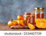 Persimmon jam. Sweet autumn homemade jam or marmalade canning preserves in a jar, with whole and cut persimmon c in the background