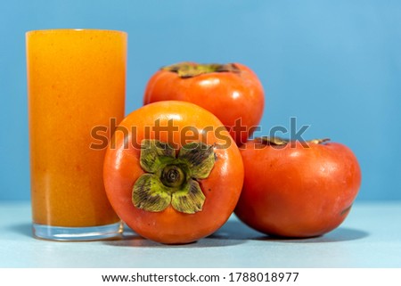 Persimmon juice and fruits on the blue background. Persimmon juice has a reserve of various phytochemicals such as catechins and polyphenolic antioxidants. Detox and refreshing drink.