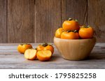 Persimmons or Persimon fruits in wooden bowl with slice isolated on old wooden table background.