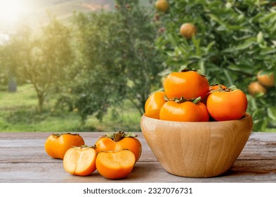 Persimmones o frutos de Persimon en tazón de madera sobre una vieja mesa de madera con fondo de plantación de árboles de persimón.