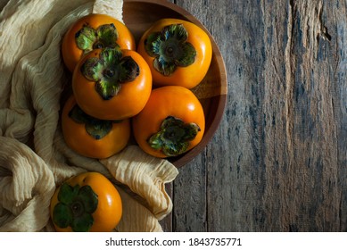 Persimmons with thin lightweight fabrics in a wooden tray on a rustic wooden background.