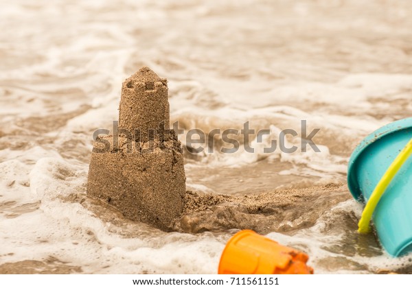 Persistent tower of the sand castle washes away in\
the sea water.