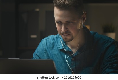 Persistent young man with earphones working at laptop indoors, concentrating and deep in thought while being productive