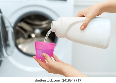 Person adding liquid laundry detergent to the washer, close up. Female hand holding laundry detergent in front of open washing machine - Powered by Shutterstock