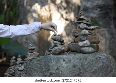 A person adding a small stone to a stack of wishing stone pagodas