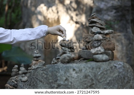 A person adding a small stone to a stack of wishing stone pagodas