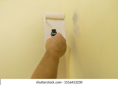 Person Appplying White Paint On Yellow Wall Using Roller Brush. Home Renovation Concept.