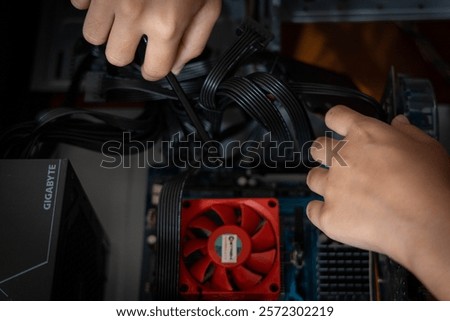 A person assembles a computer, handling cables inside a case with a Gigabyte power supply and a motherboard with a red cooling fan.