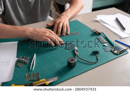 Person is assembling circuit boards using tools and a ruler on a work table with green matting.
