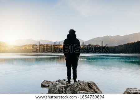 Person from behind looks at beautiful lake at sunrise.
Relaxed, peaceful, thoughtful, happy and free at the mountain lake.